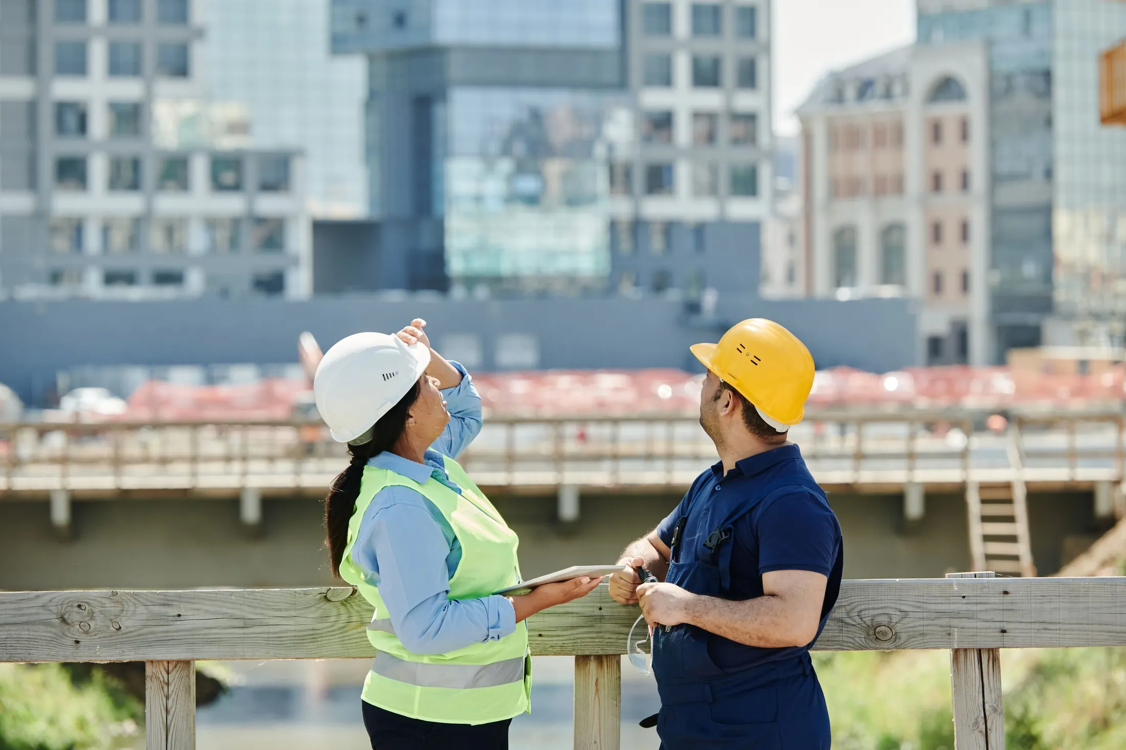Two engineers in safety helmets reviewing plans at a construction site